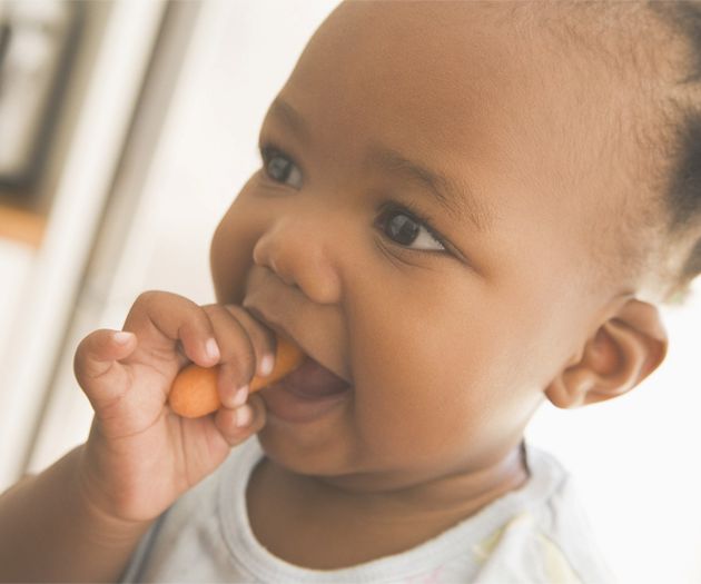 Baby holding a baby carrot in its mouth and smiling